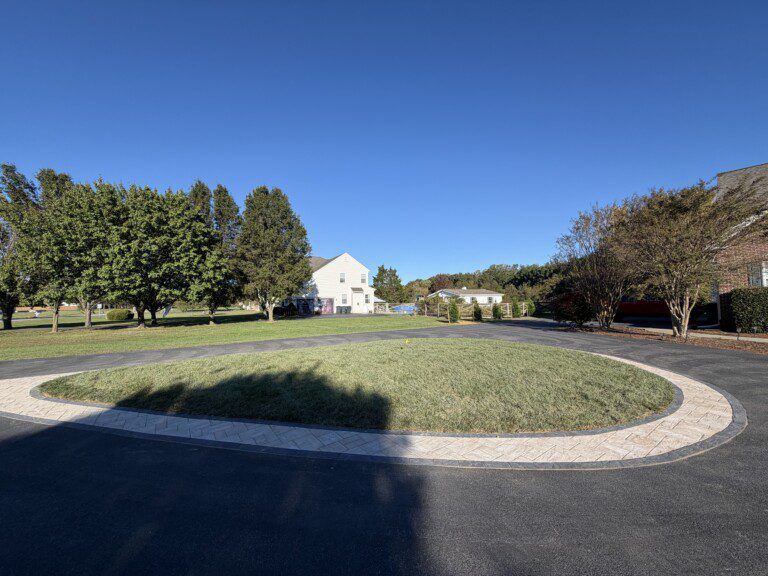 Circular driveway with a grassy center, surrounded by trees and a building against a blue sky.