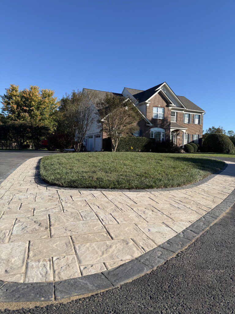 Brick home with a circular driveway and grass island. Clear, blue sky.