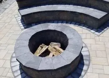 Fire pit with stacked wood surrounded by stone patio, curved stone steps in background.