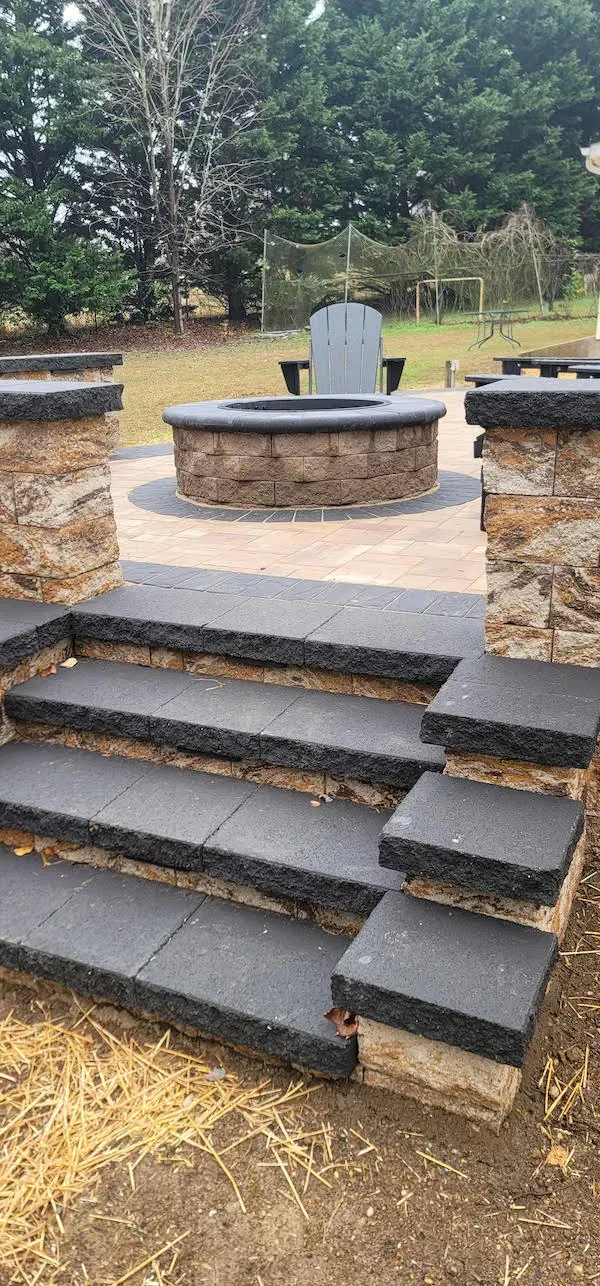 Stone fire pit and seating area with steps and pillars in a yard.
