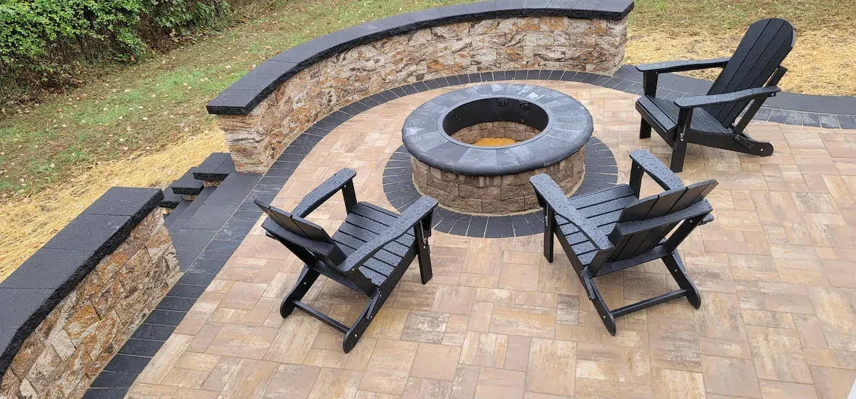 Patio with fire pit, stone wall, and three black Adirondack chairs.