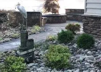 Stone garden path with a heron statue, surrounded by rocks and shrubs.