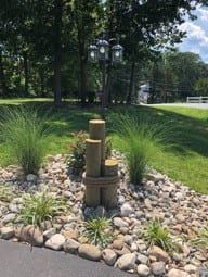 Landscaped area with decorative wooden posts, rocks, and ornamental grasses. Lamp post in background.