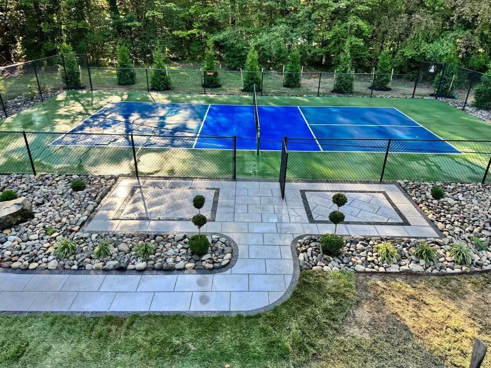 Pickleball court with blue and green surfaces, black fencing, and landscaped walkway.