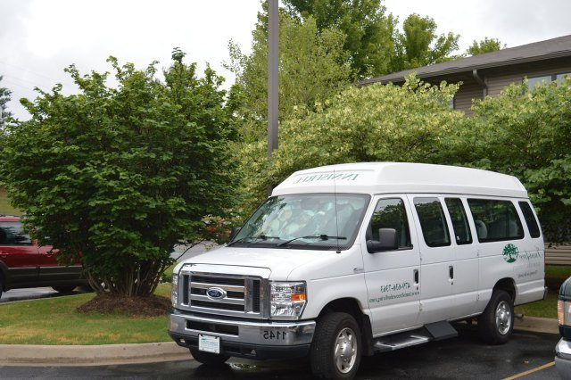 White van with “Care-N-Share” logo parked in front of a building with greenery.