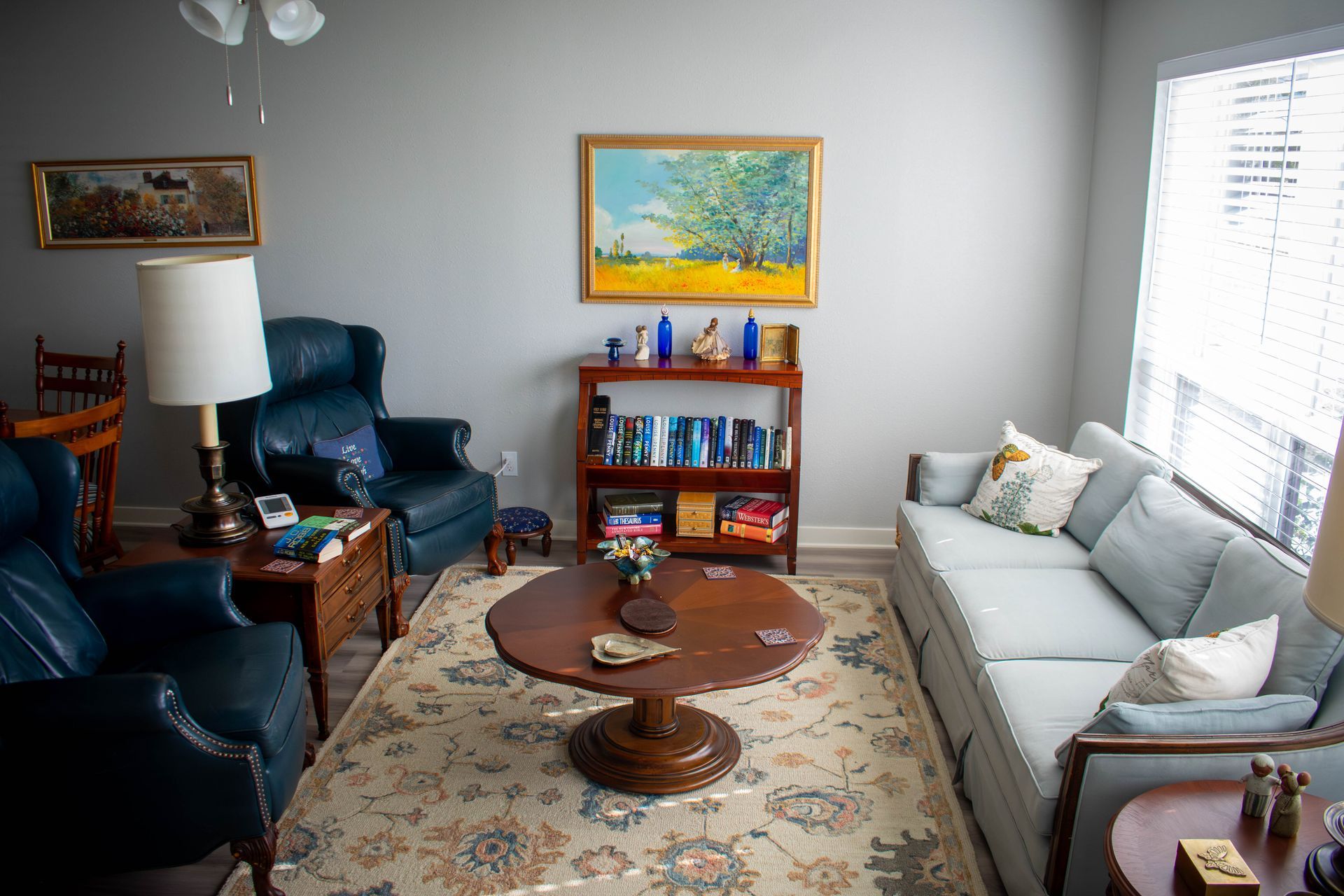 Living room with blue furniture, art, books, and a round coffee table on a patterned rug.