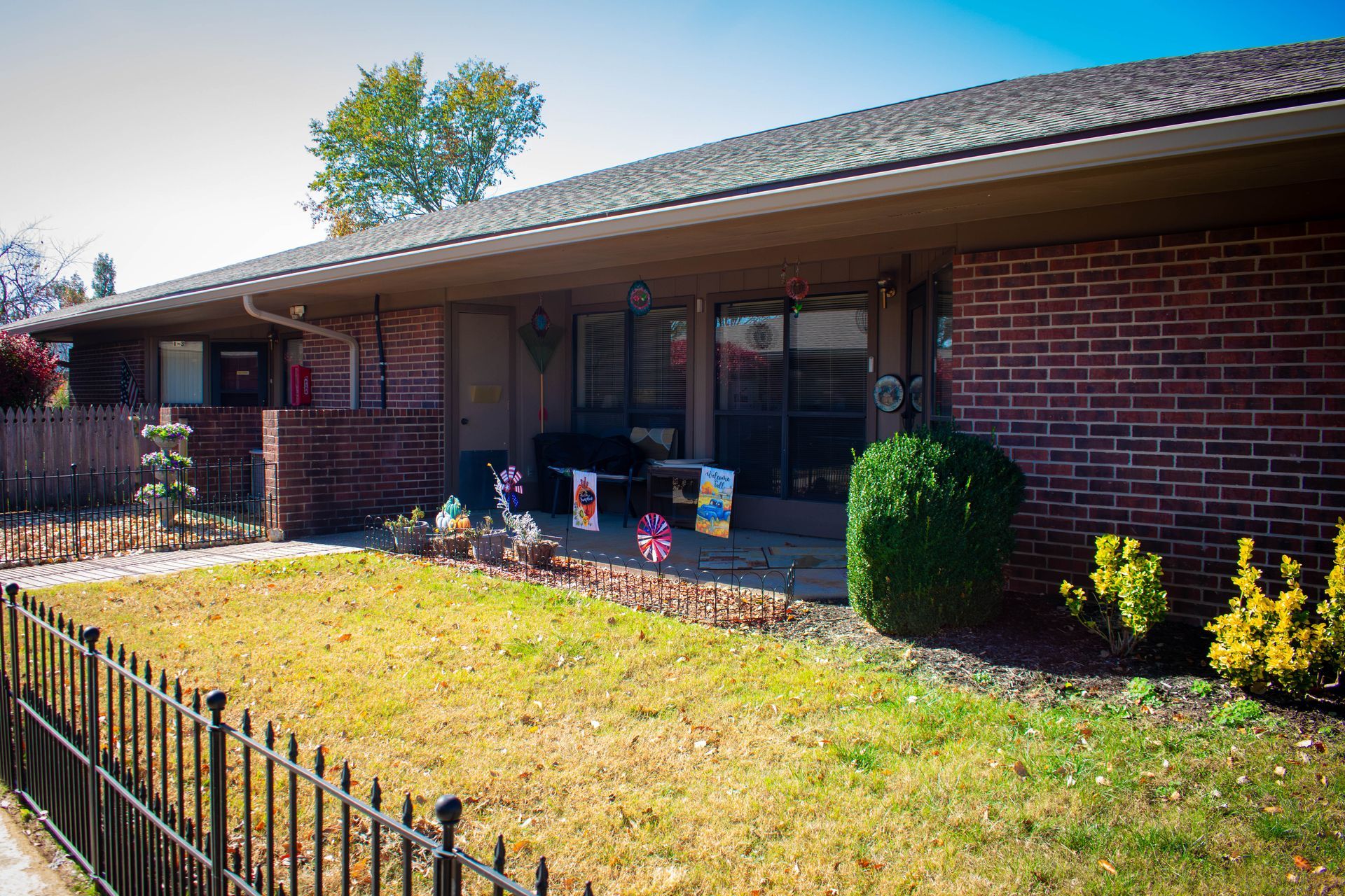Brick building with a low roof and small porch, black fence, and small yard with some decorations.