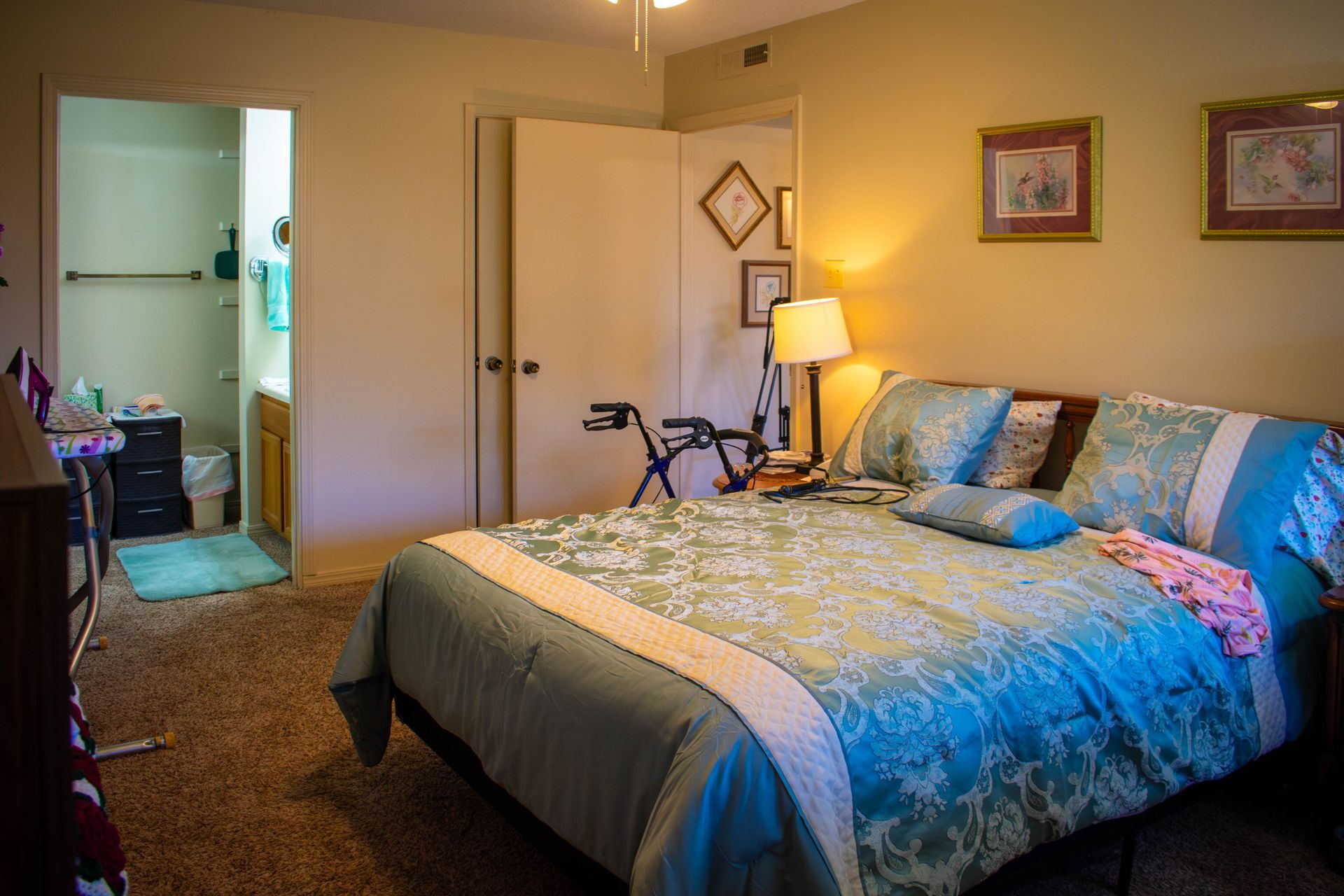 Bedroom with double bed, adjacent bathroom, walker, and framed art. Turquoise and brown color scheme.