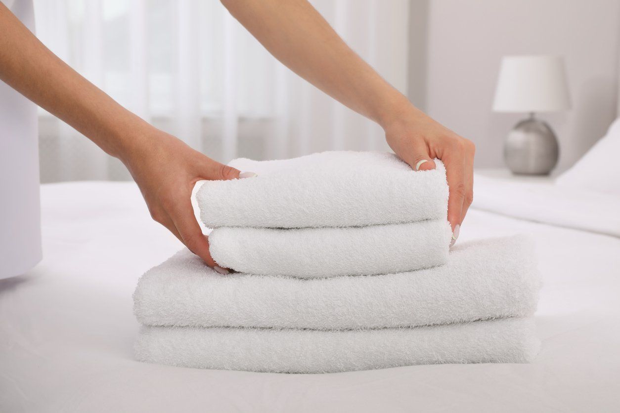 Hands stacking clean, white towels on a bed in a hotel room.