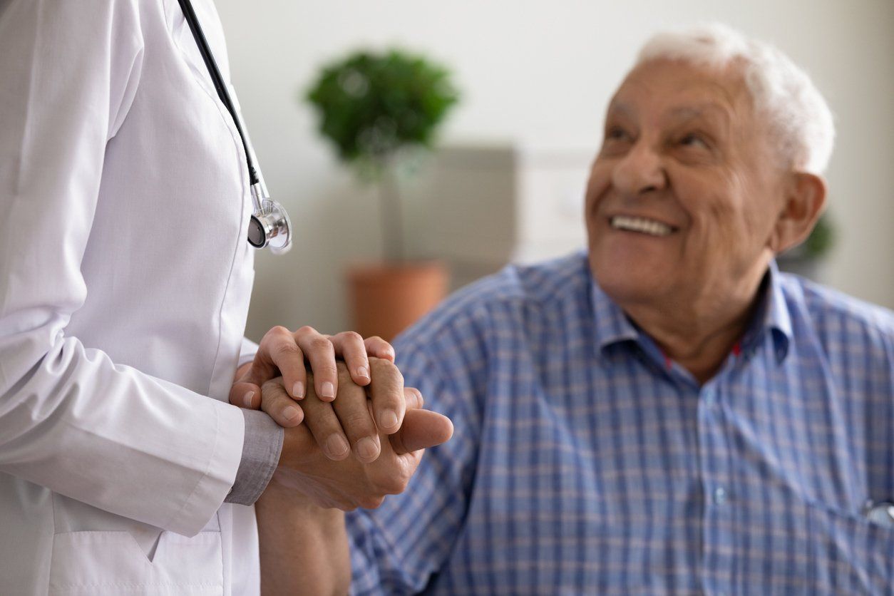 Doctor holding elderly person's hands; both are smiling in a medical setting.