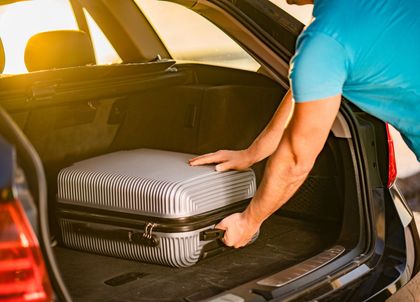 Person loading a striped suitcase into a car trunk at sunset