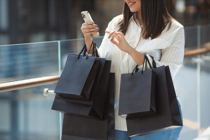 Woman carrying black shopping bags while looking at her phone in a mall.