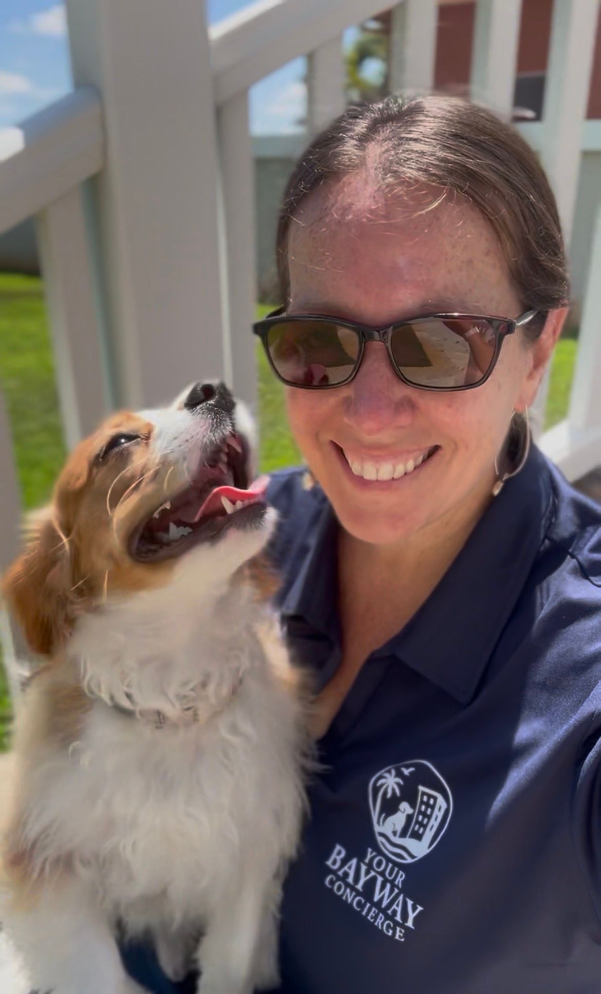 Woman smiling with sunglasses and dog on porch, both looking at each other