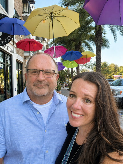 Two people smiling on a city sidewalk under colorful umbrellas