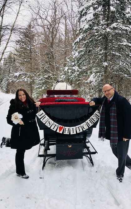Two people stand beside a red and black piano in a snowy park with a banner draped across it.