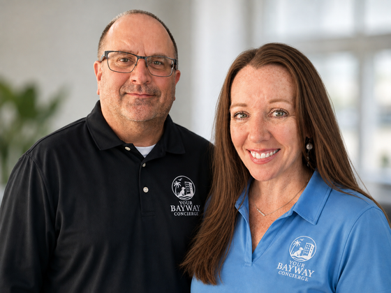 Two people standing indoors, smiling at the camera in black and blue collared shirts.