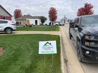 An Eagle Ridge Roofing sign sits on a residential lawn near a truck and a work trailer at a construction site.