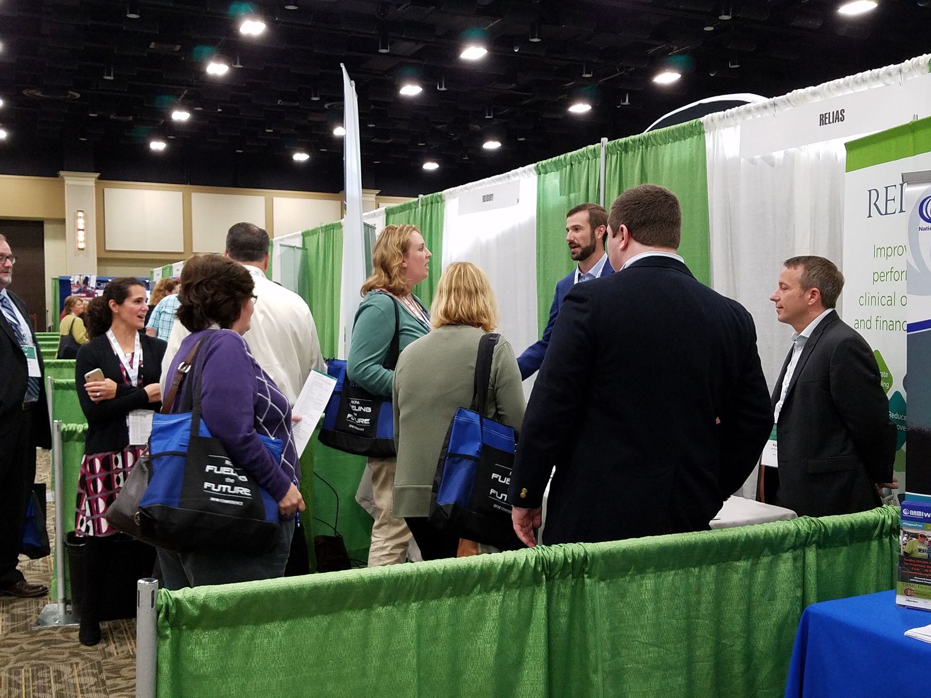 People networking at a trade show booth with green curtains and white banners in a convention hall
