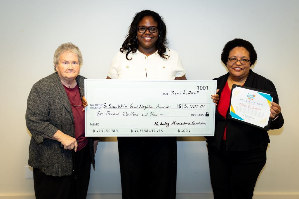 Three women hold a large check and an award certificate. They stand in front of a white background.