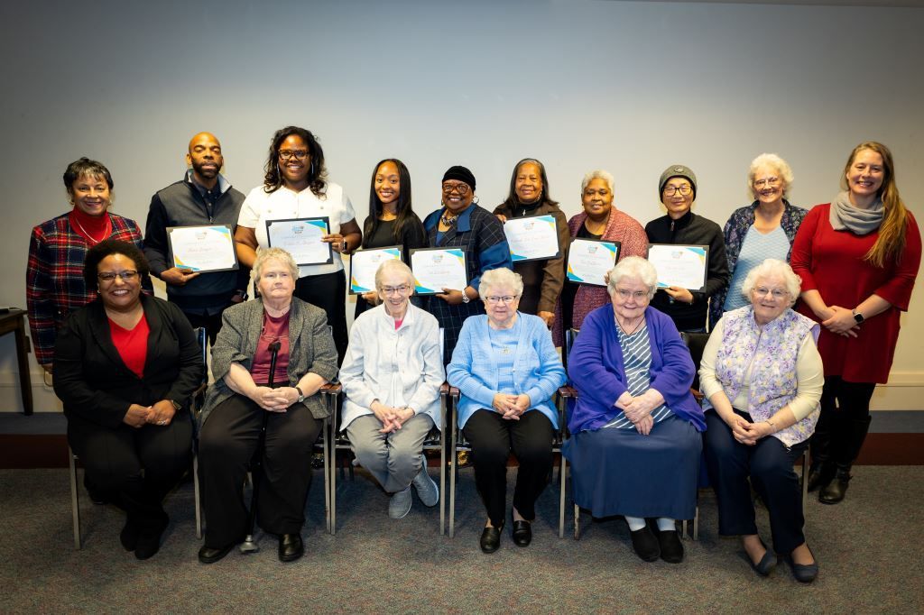 Group of people holding certificates, smiling, indoors. Some are seated, some standing.