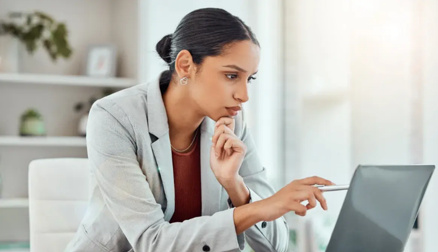 Woman in a light blazer using a laptop and pointing at the screen in a bright office
