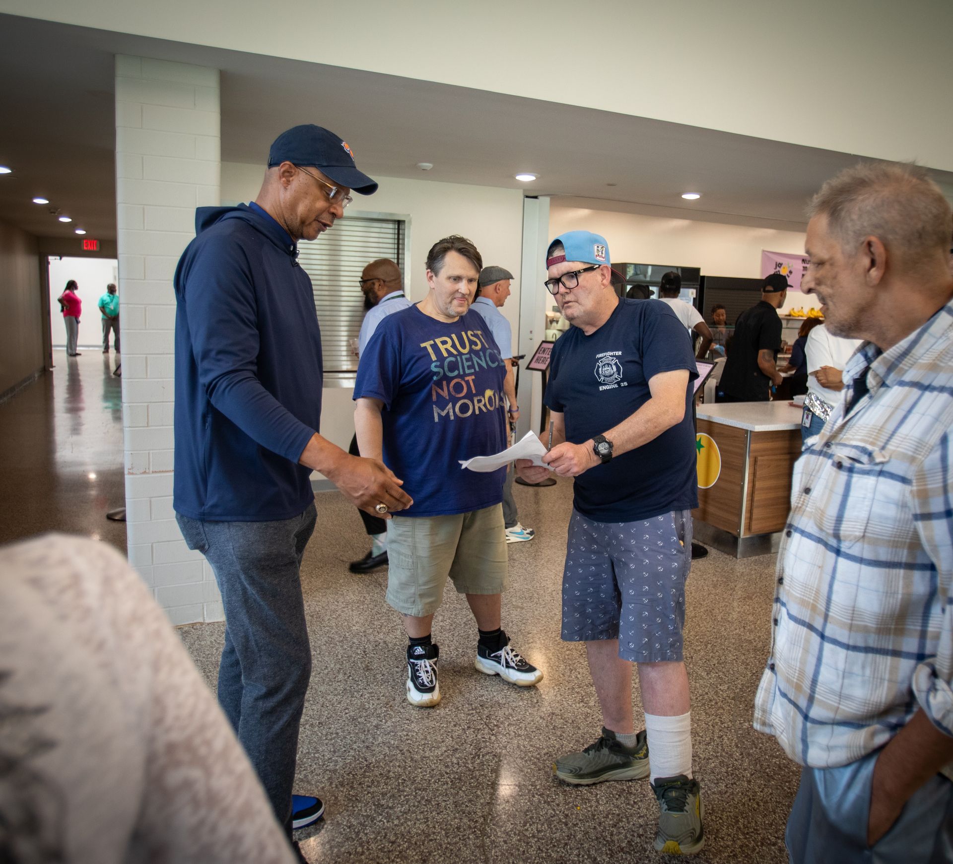 People chatting in a bright lobby, one man showing papers to three others