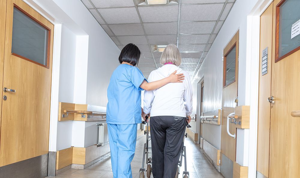 Nurse supporting a patient down a bright hospital corridor