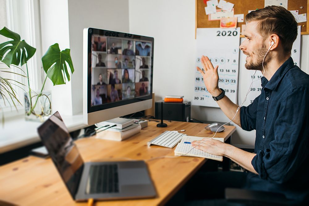 Man smiling and waving at screen showing meeting attendees