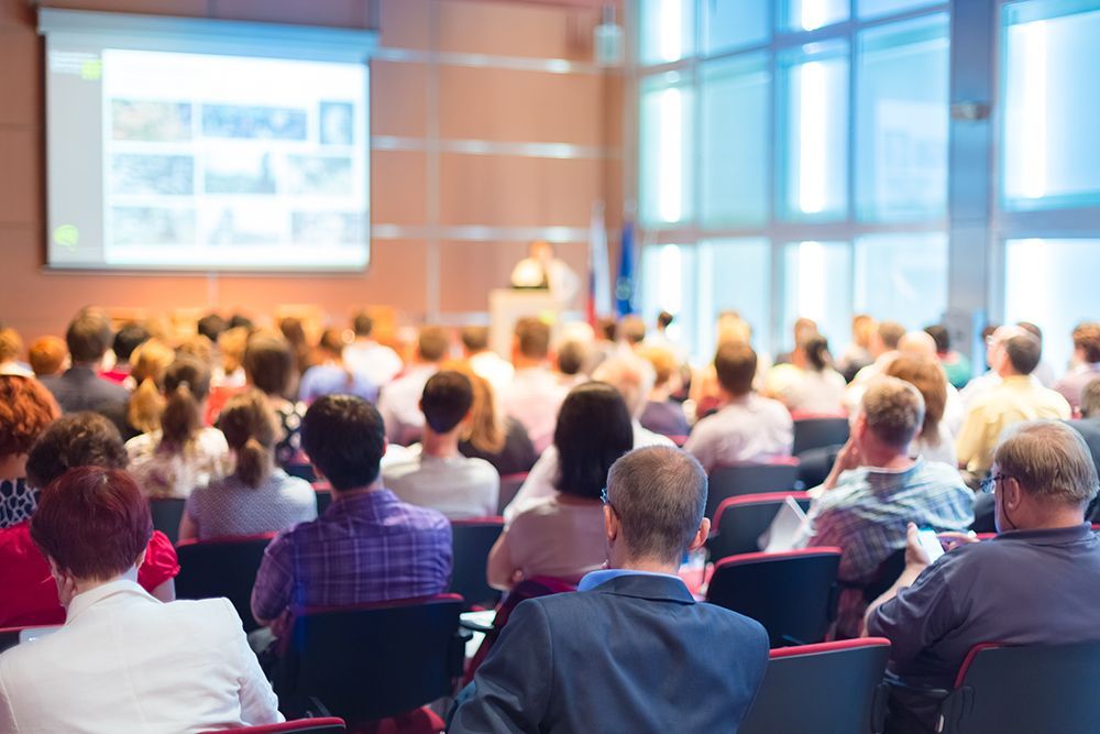 Attendees in conference room listening to speaker and looking at PowerPoint presentation
