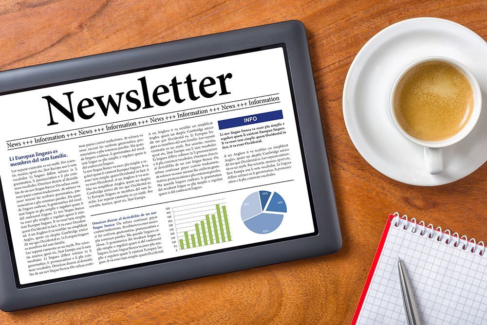 Tablet next to cup of coffee and a notepad with 'Newsletter' at top of screen