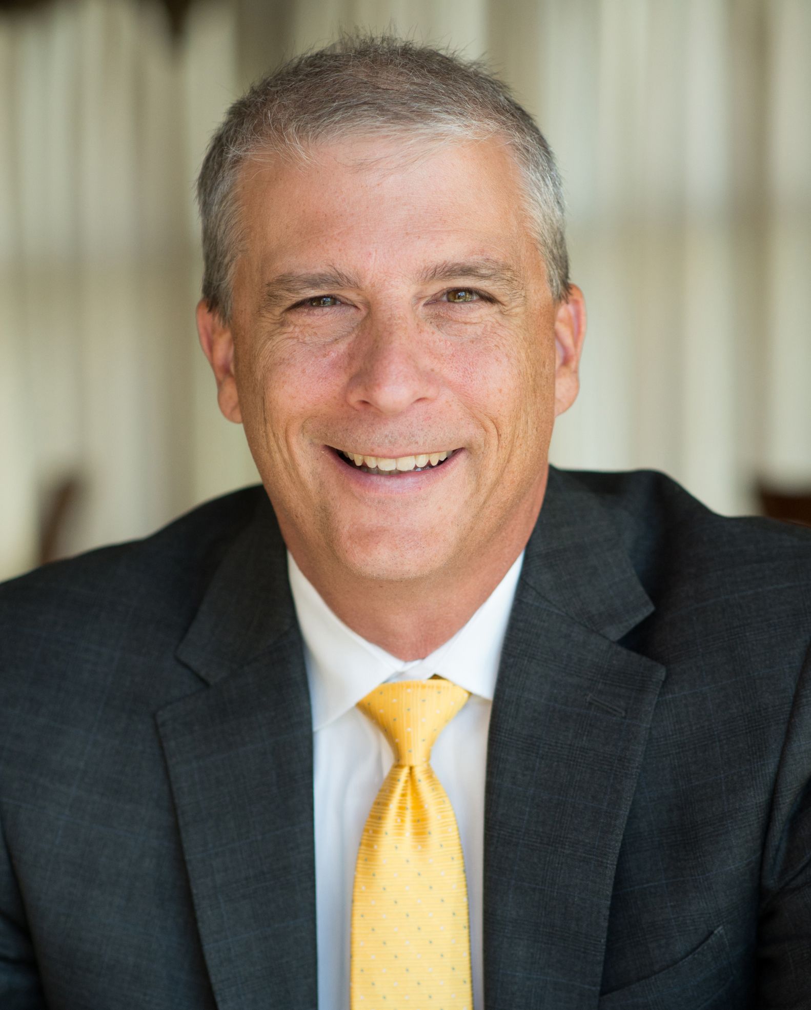 Keynote Presenter Name Smiling man in a dark suit and yellow tie, posed indoors against a blurred background.