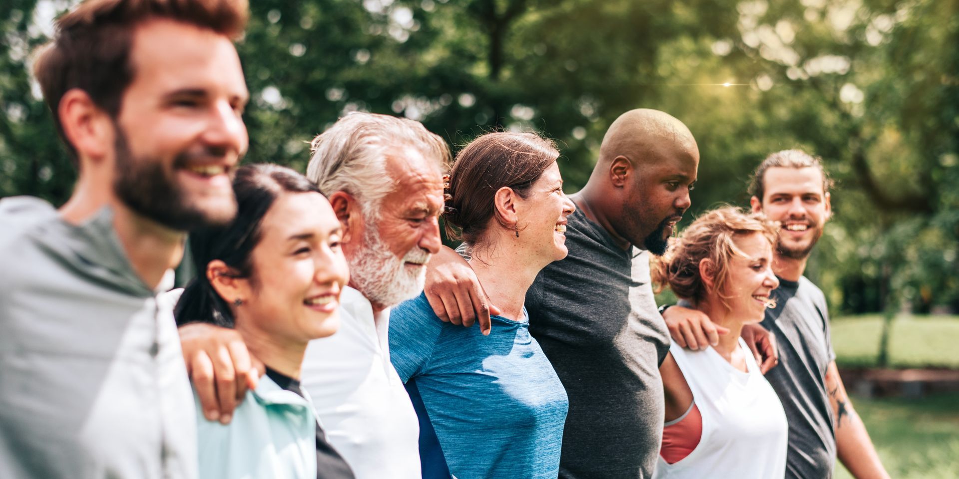 A diverse group of people walking together outdoors in a park, smiling and linked arm-in-arm.