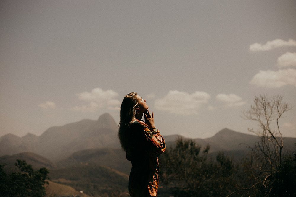 A person standing in silhouette against a mountain landscape, looking upward toward the sky.