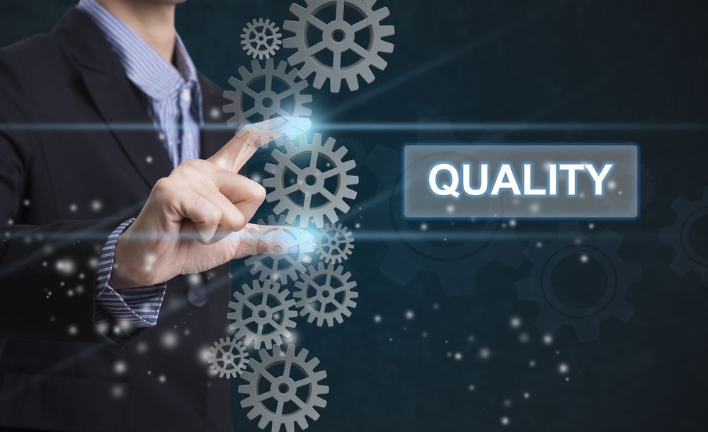 Businessman touching digital gears beside “QUALITY” on a dark blue background
