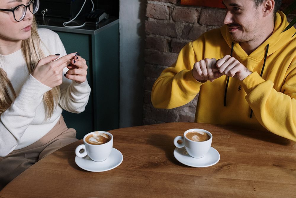Two deaf individuals using sign language to communicate while siting at a table with cups of coffee