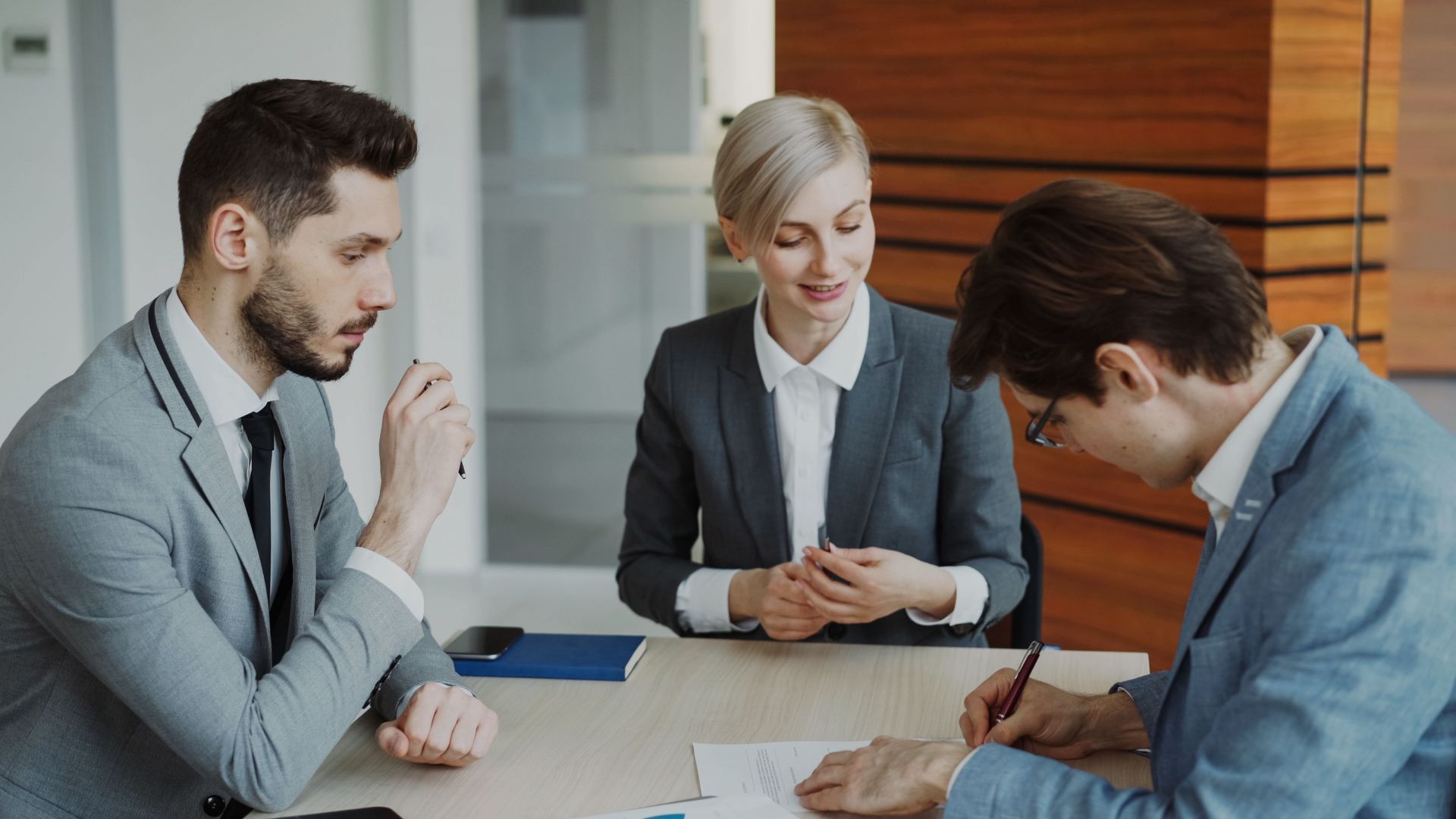 Two men and one woman in business suits discussing business at a table