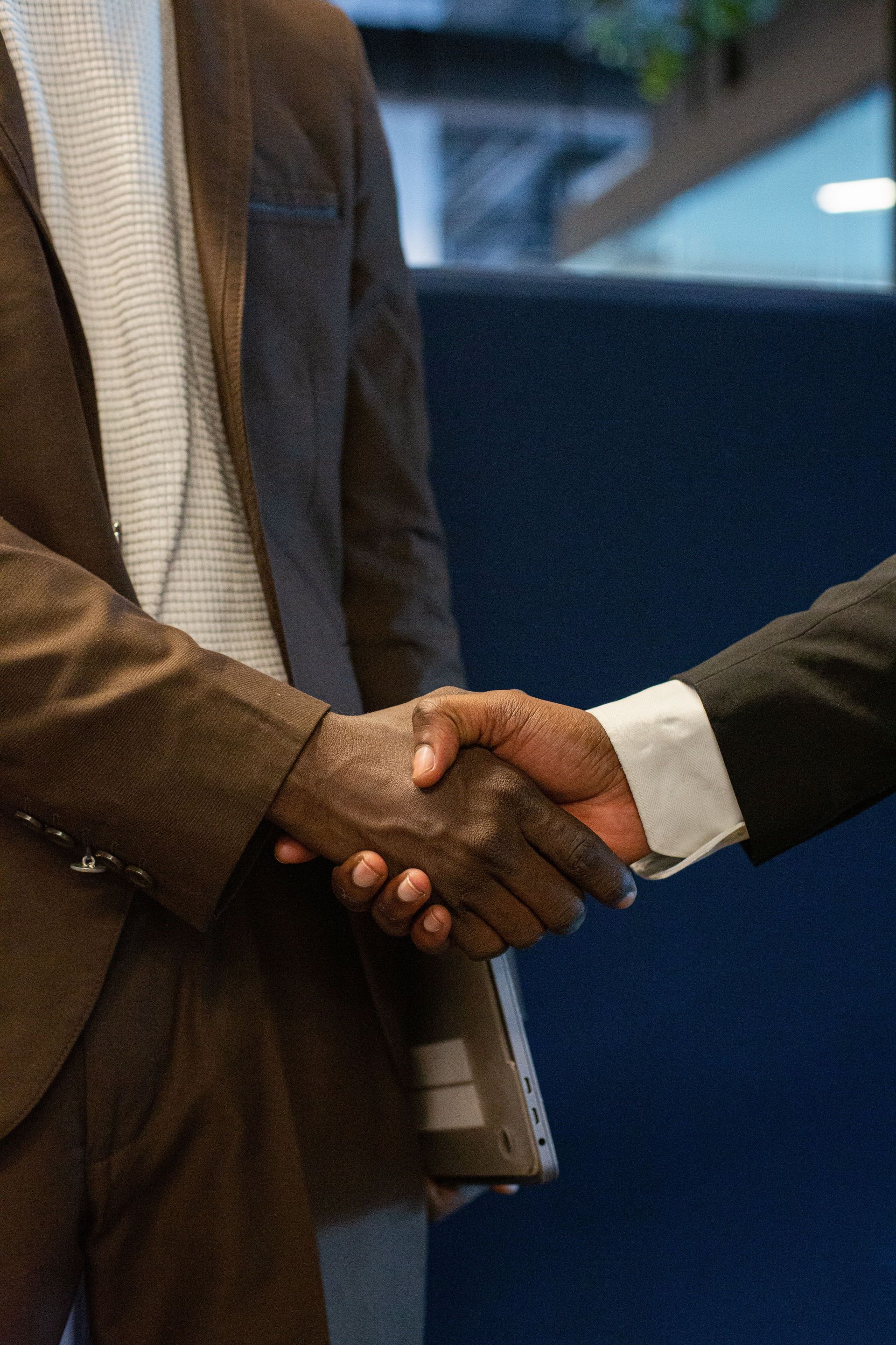 Two people in suits shaking hands in an indoor setting.