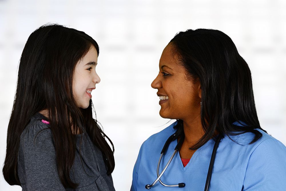 Black nurse smiling at white child in doctor's office setting