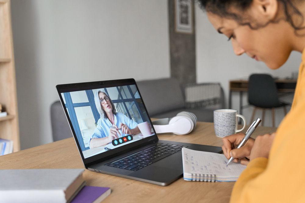 Person taking notes while listening to speaker on laptop 