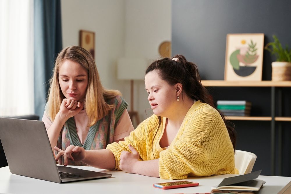 Woman assisting another woman with IDD with working on a laptop