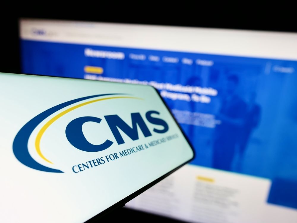 Phone with CMS logo in front of computer showing CMS website