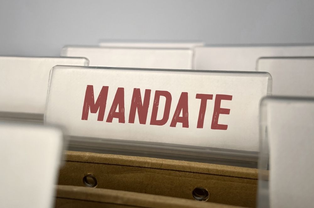 File tabs labeled “MANDATE” in red text on a beige filing rack