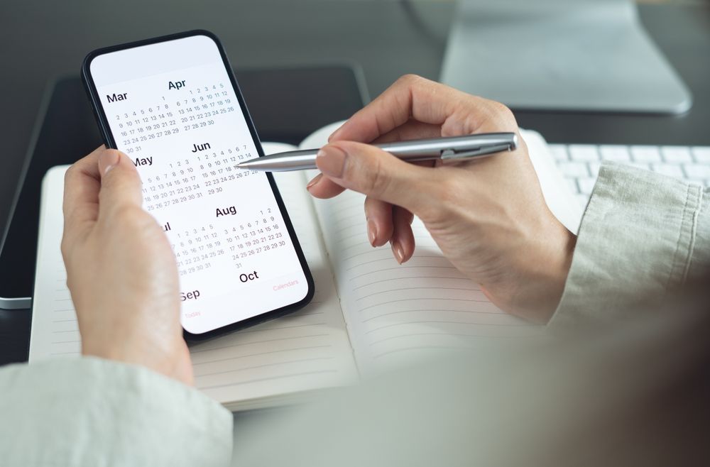 Person holding phone showing calendar, using pen to point at a specific date