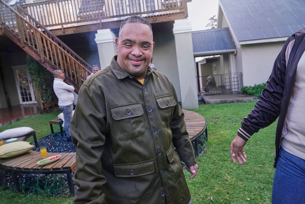 Person with IDD smiling at camera and working in a backyard with others