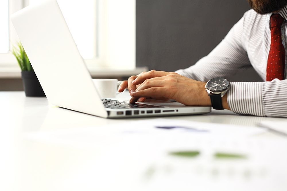 Man in button-up shirt and tie at desk typing on laptop