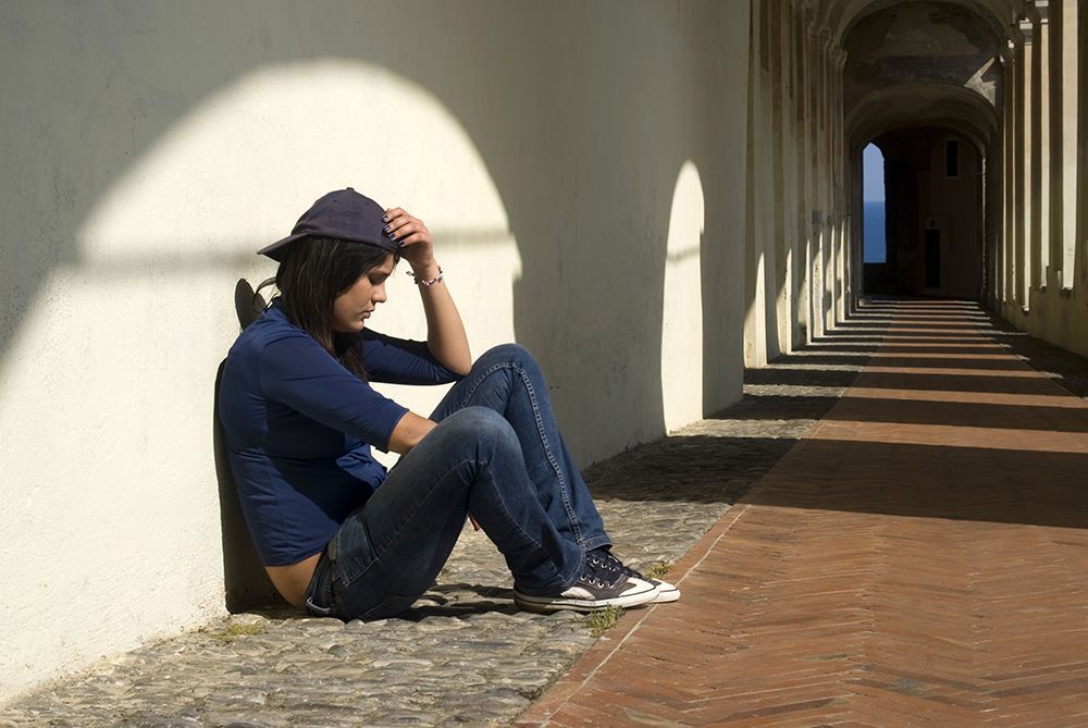 Woman leaning against wall with sunlight on her appearing depressed and frustrated 