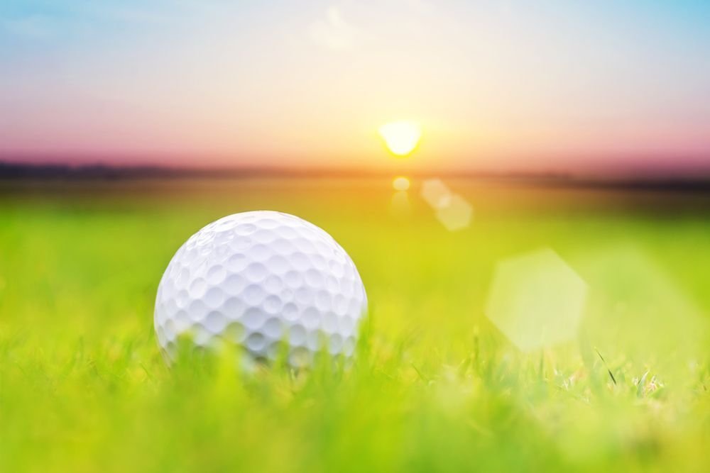 Golf ball in green grass at sunrise with a blurred horizon and warm sunlight