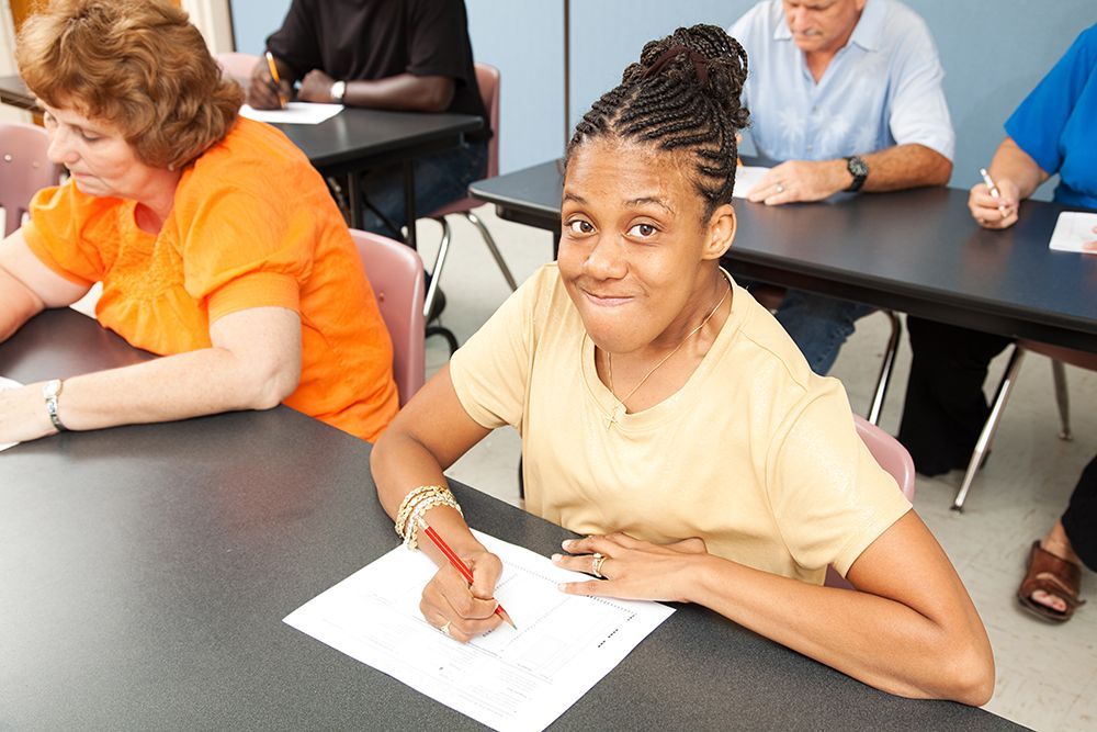 Black woman filling out paperwork for job interview with others at table around her