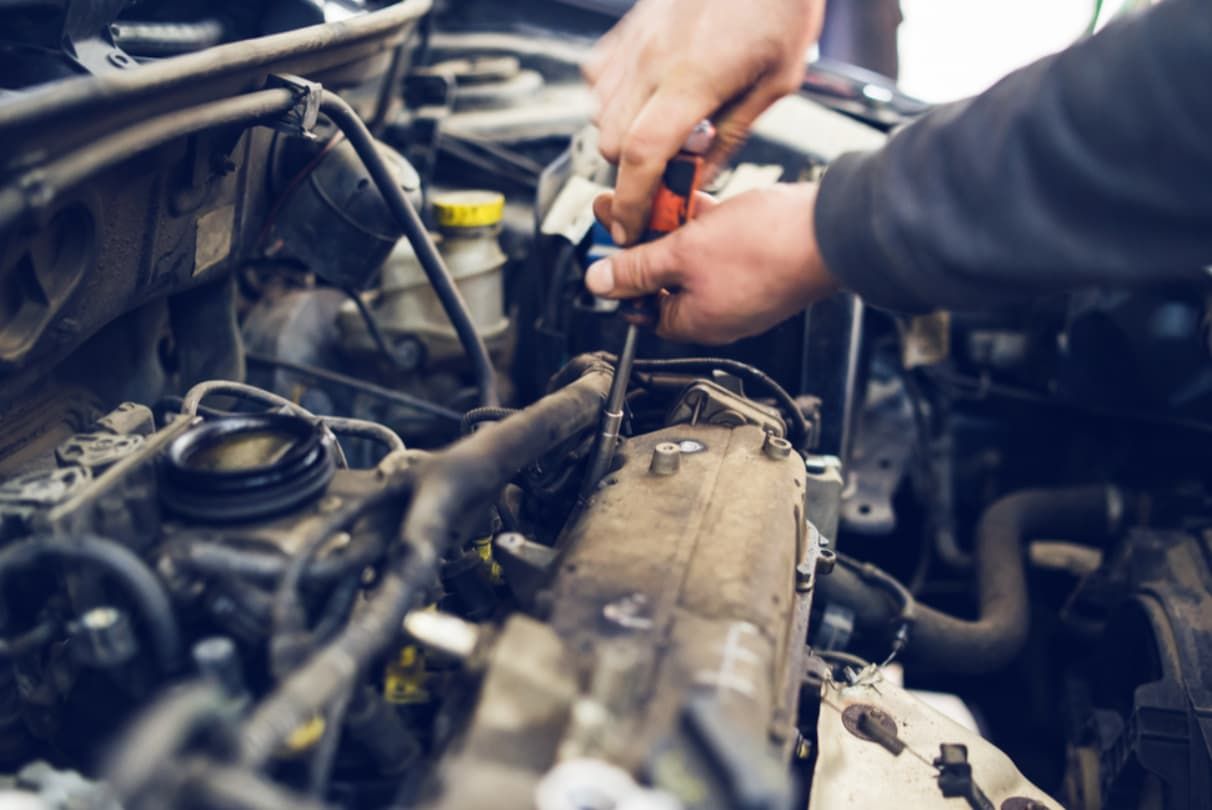 A Man Is Working On The Engine Of A Car With A Screwdriver — North Queensland Diesel Tune In Kirwan, QLD