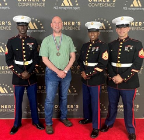 A man with a medal stands with three Marines in uniform at a conference with a red carpet.